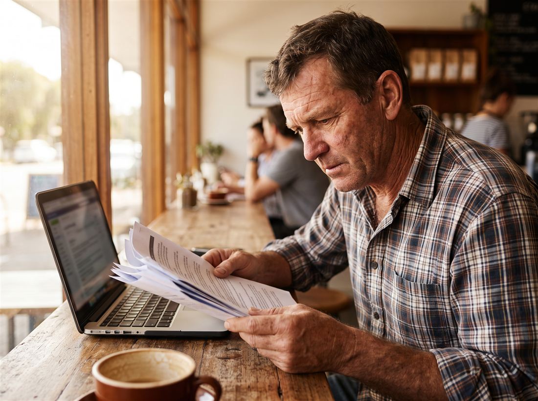 A business owner reviewing a printed ad spend report next to his laptop at a cafe