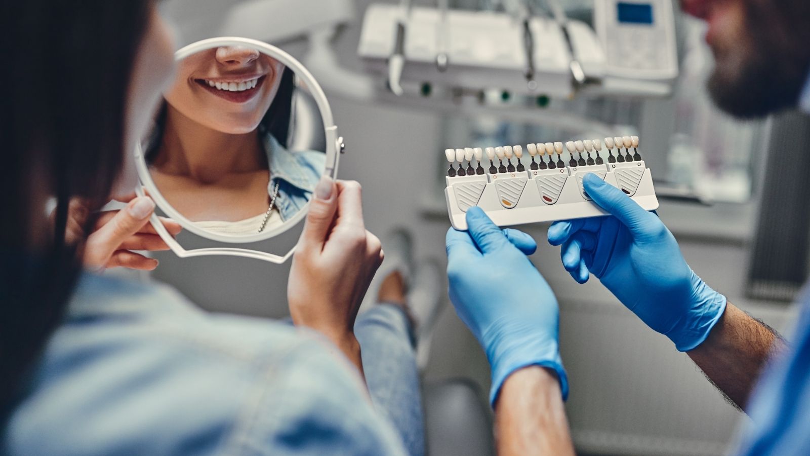 Dentist and patient reviewing tooth shade options together, patient smiling in a hand mirror